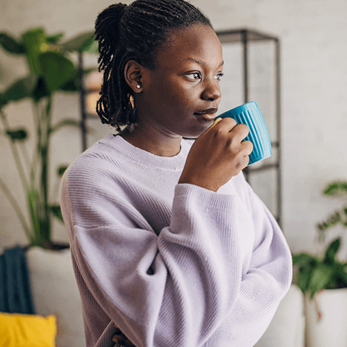 Young woman patient of Balanced Mental Health of Arizona wearing a purple sweatshirt and holding a cup of coffee.