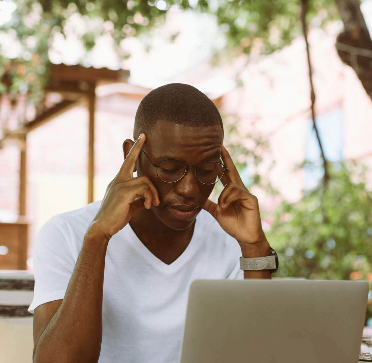 Young man, a patient of Balanced Mental Health of Arizona, with glasses sitting at a computer with his fingers on his temples in frustration.