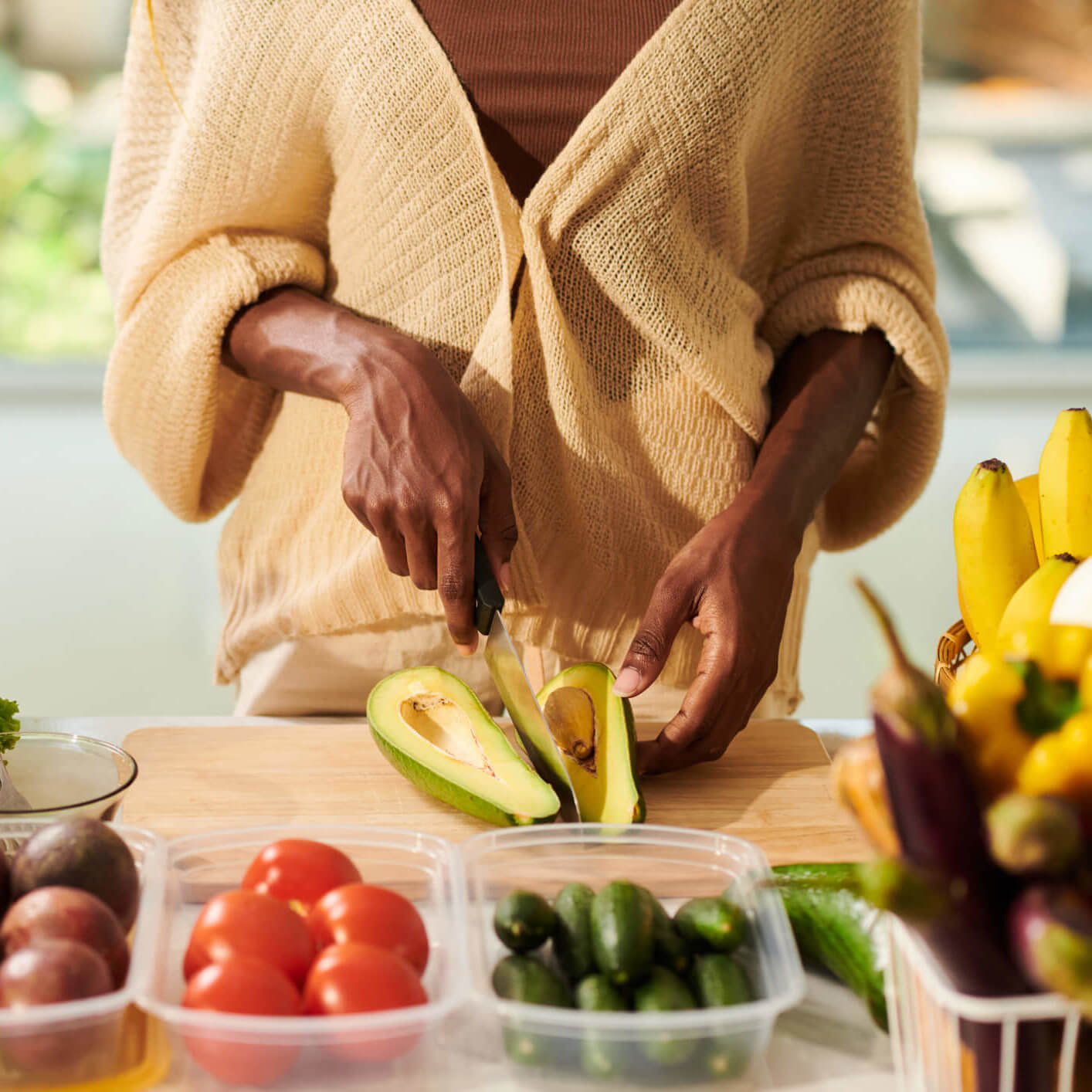 Hands of a young woman cutting an avocado and other vegetables on a cutting board.