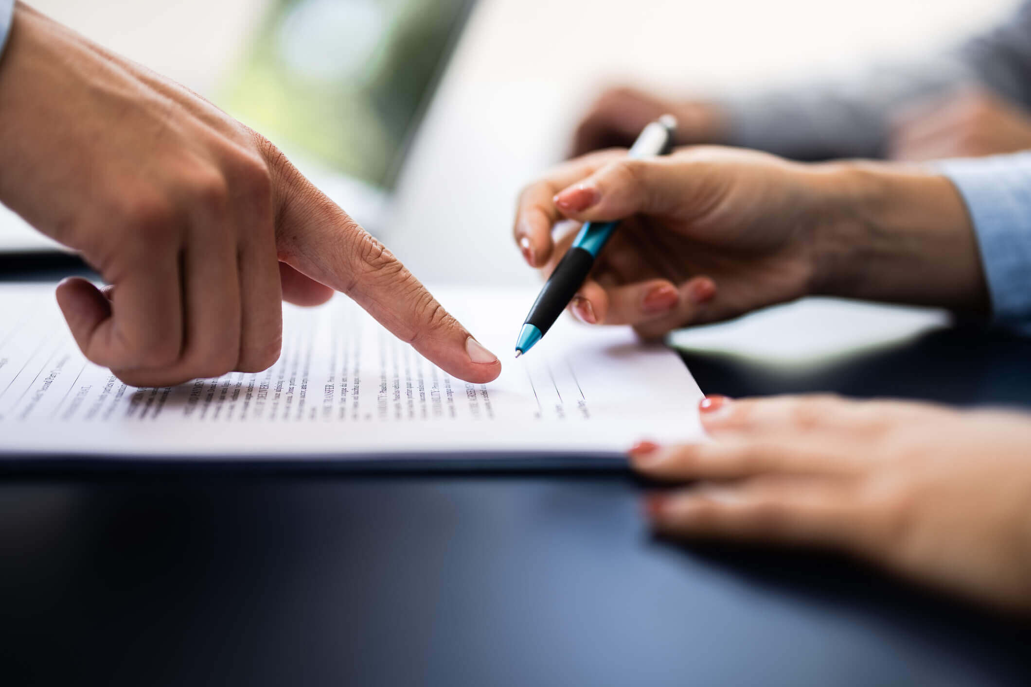 Finger pointing at a spot on a document for a pair of hands holding a pen to sign.