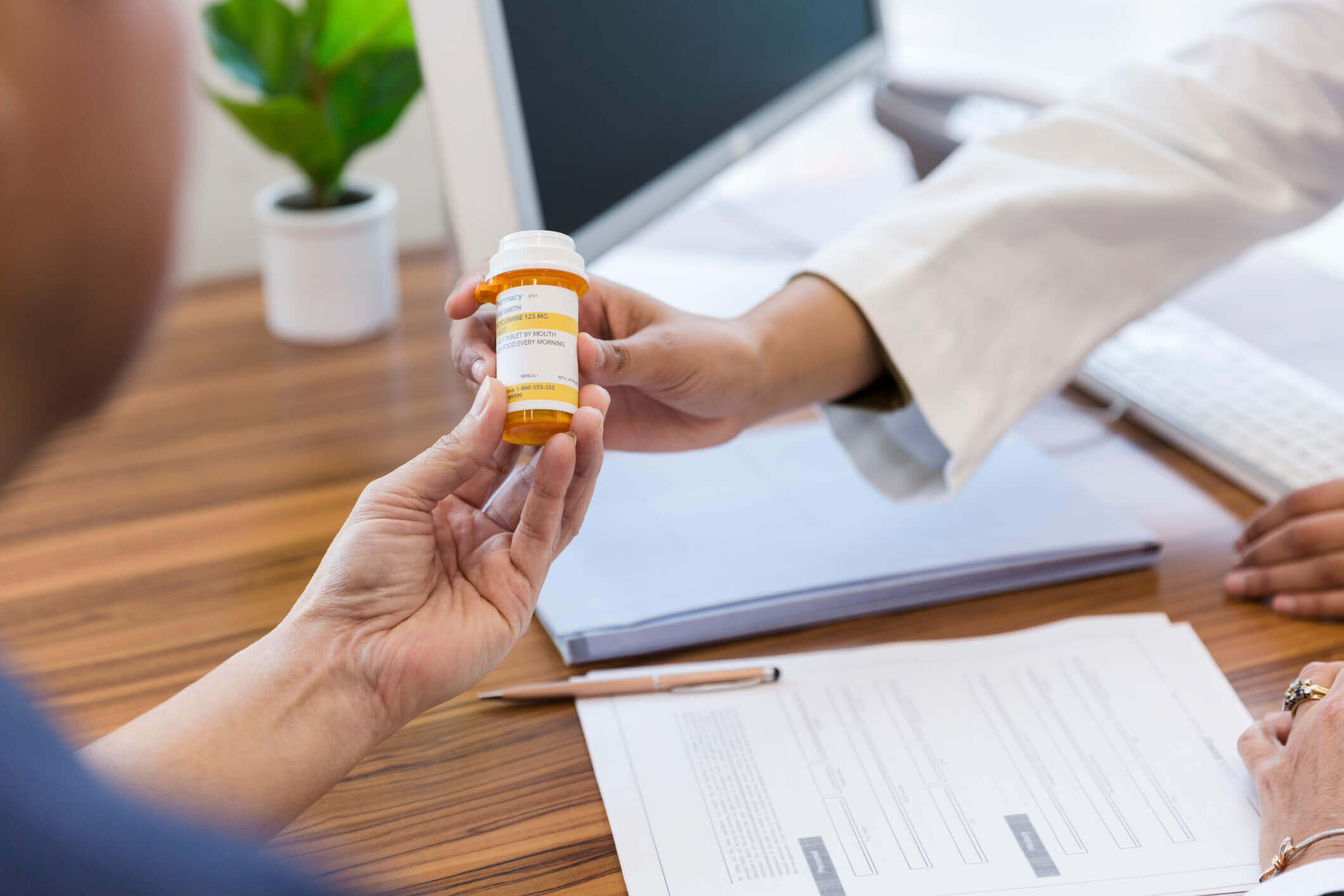 Hand of a medical professional wearing a white coat handing a prescription pill bottle to a patient.