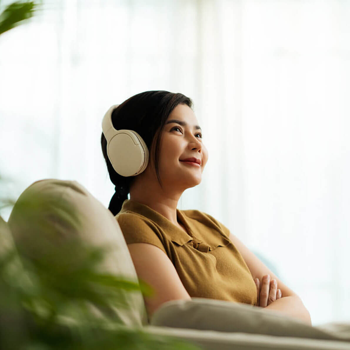 A young women patient of Balanced Mental Health of Arizona sitting on her couch wearing over-ear headphones and smiling