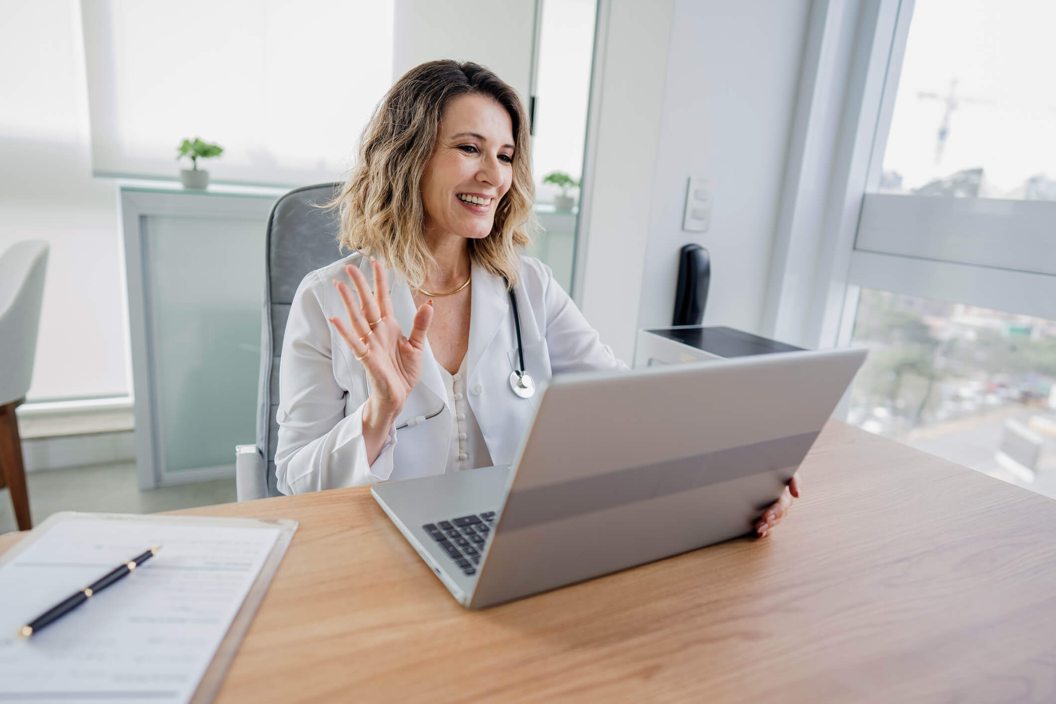 Young medical professional waving to a patient via a virtual doctor's visit.