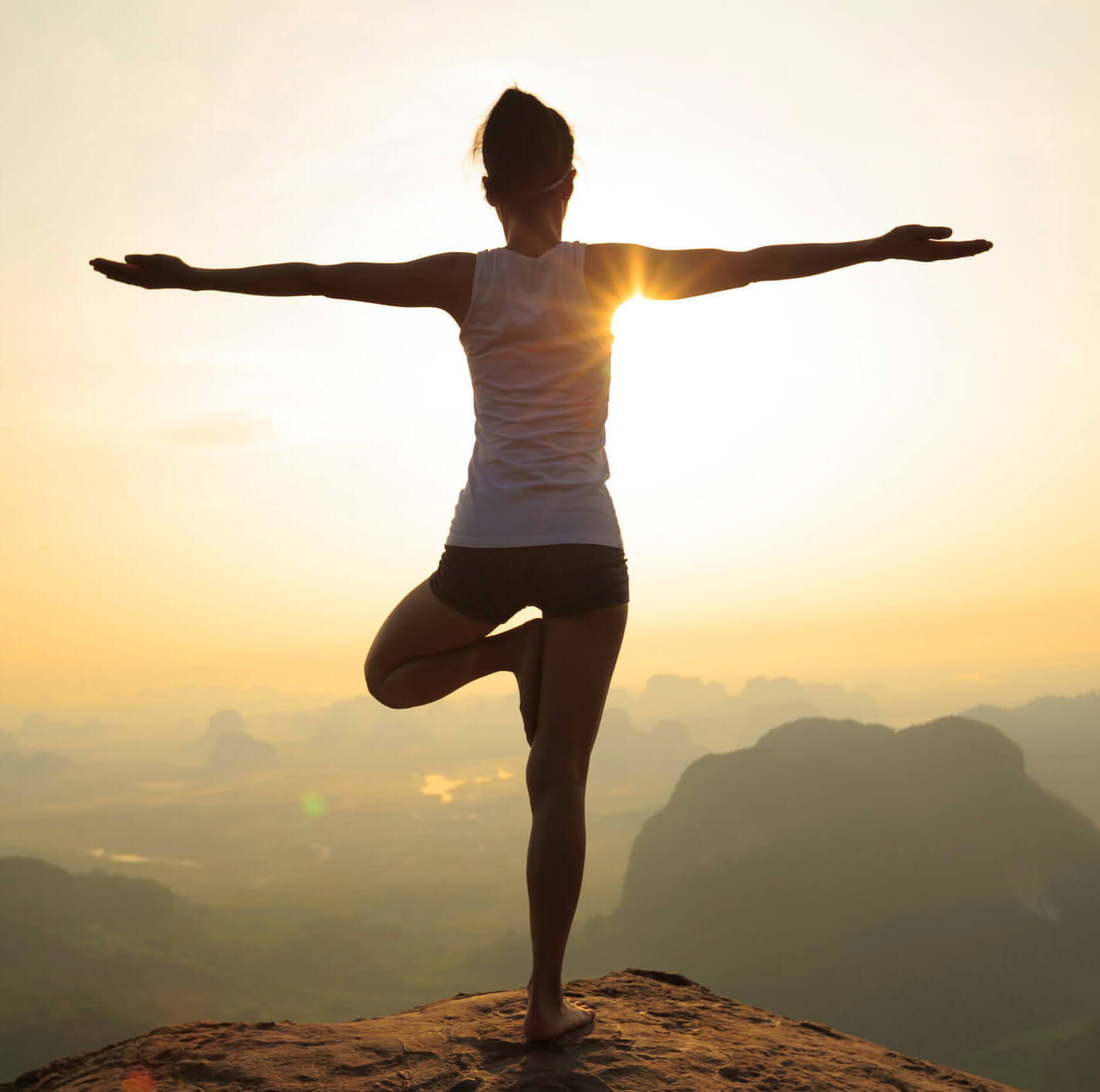 Silhouette of a young, athletic woman - a patient of Balanced Mental Health of Arizona - doing a yoga pose on a mountain top.