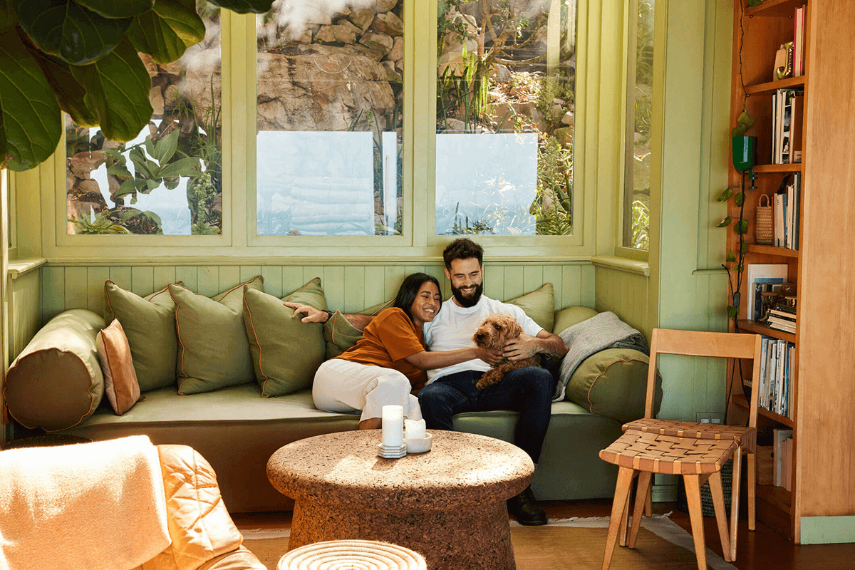 A young couple, patients of Balanced Mental Health of Arizona, sitting on a couch in their green living room petting their dog